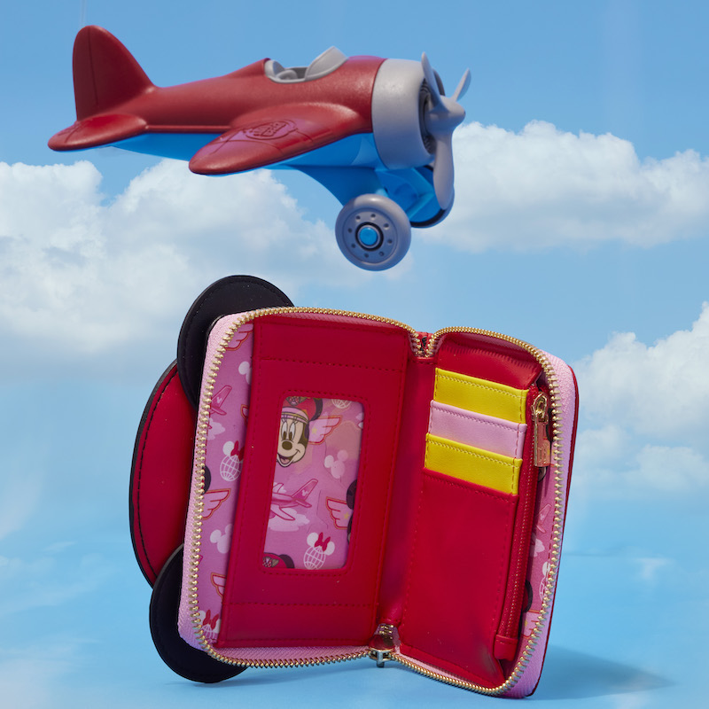 Inside look at the Limited Edition Loungefly Minnie Mouse Pilot wallet, featuring four card slots that are yellow, pink, and red, plus one clear slot for an ID. The wallet sits against a background that looks like the sky with a red and blue airplane flying above it.